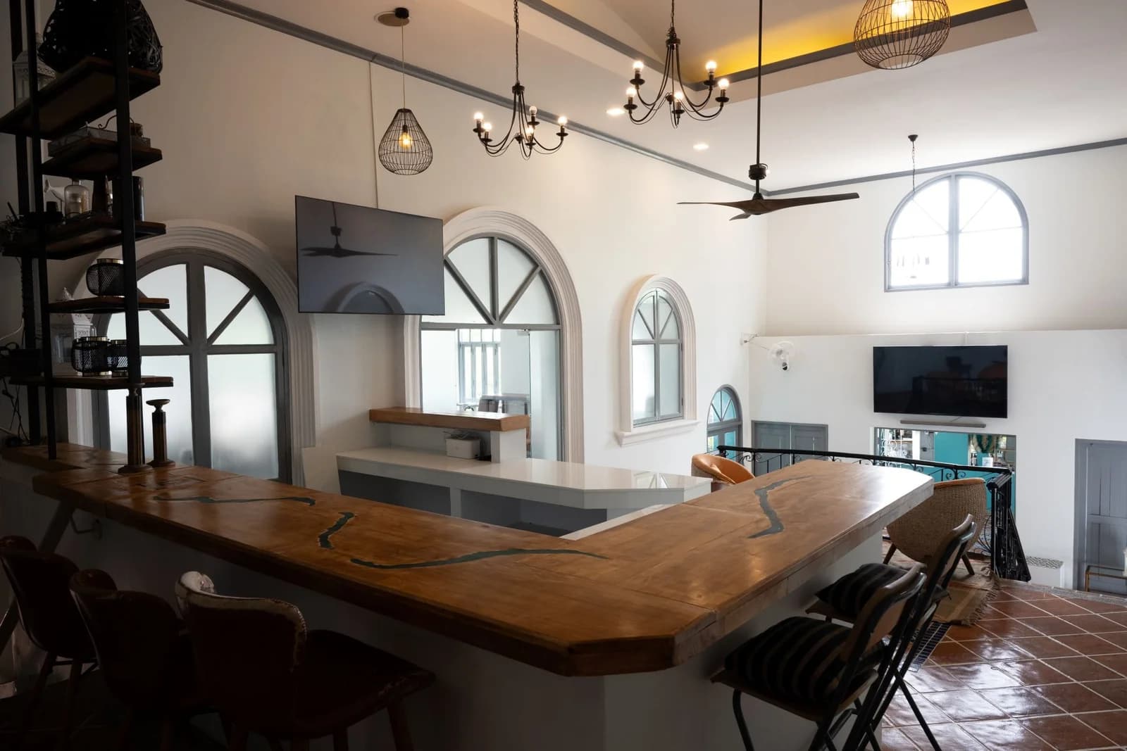Modern upper-level bar inside Soho Clubhouse Phuket featuring a wooden counter, pendant lighting, and arched windows overlooking the lounge area.