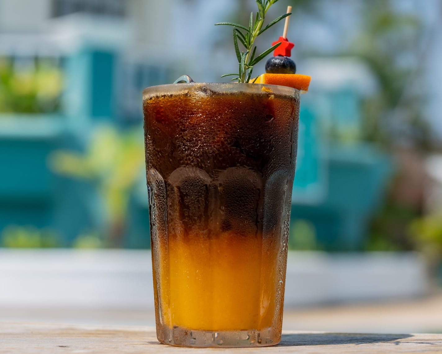 Iced orange coffee with a citrus garnish and rosemary sprig, served in a glass at SOHO Pool Club.