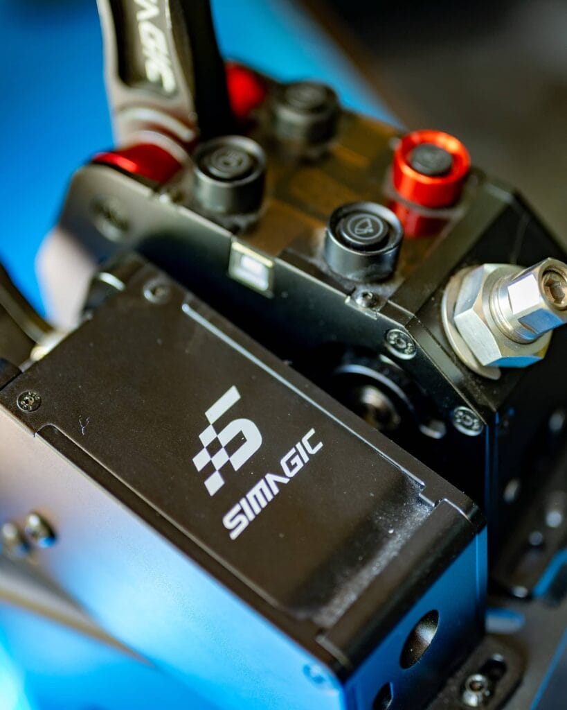 Close-up of a SimPro racing simulator pedal assembly featuring the Simagic logo, metallic controls, and red and black adjustment knobs.