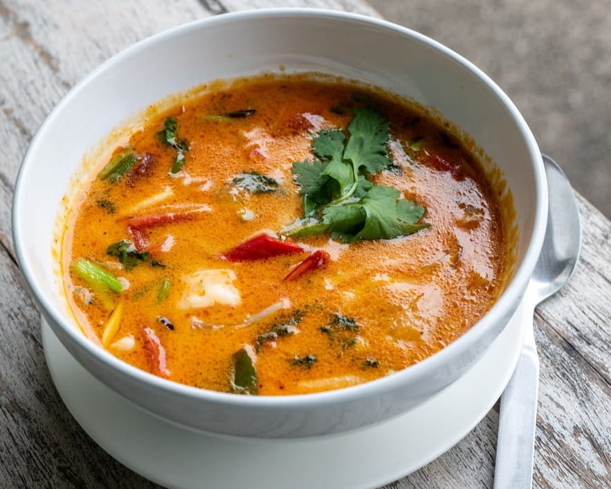 Creamy Thai tom yum soup with chili, lemongrass, herbs, and cilantro served in a white bowl.